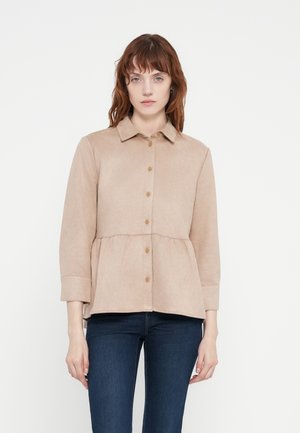 Light beige button-up shirt with a peplum waist, long sleeves, and a collar. Made from soft fabric with a smooth texture.