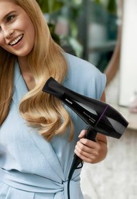 Asciugacapelli Philips, 2200W, con un elegante corpo nero, dettagli in viola e un beccuccio affusolato. Utente con capelli mossi, indossa un indumento azzurro chiaro.