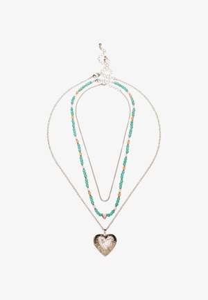 Collier à trois couches avec des chaînes en argent, des perles turquoise et orange, et un pendentif en forme de cœur gravé au centre.