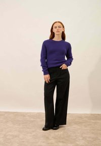 Violetti teksturoitu neulepaita raglan-hihoilla, yhdistettynä korkeavyötäröisiin mustiin leveälahkeisiin housuihin ja mustiin kenkiin. Neutraali tausta.