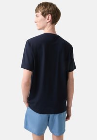 Mørkeblå kortærmet T-shirt lavet af glat stof, med rund hals. Iført med lyseblå shorts, der viser en afslappet bagside.