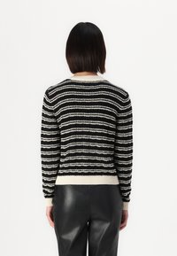 Zwart-wit gestreepte trui met een gestructureerde brei, geribde boorden en een crèmekleurige kraag, gedragen met zwarte leren broek.