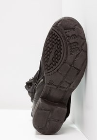 Bota de cuero negro con un diseño estructurado, suela de goma con agarre texturizado y detalle de cremallera metálica en el lateral.