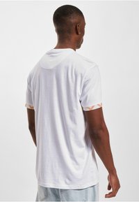 White short-sleeve t-shirt with a smooth texture, featuring patterned accents in orange and pink on the sleeves; casual fit.
