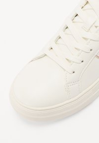 Sneaker bianca in pelle con lacci piatti, punta rotonda, suola in gomma testurizzata e branding discreto sul lato. Design liscio e minimalista.