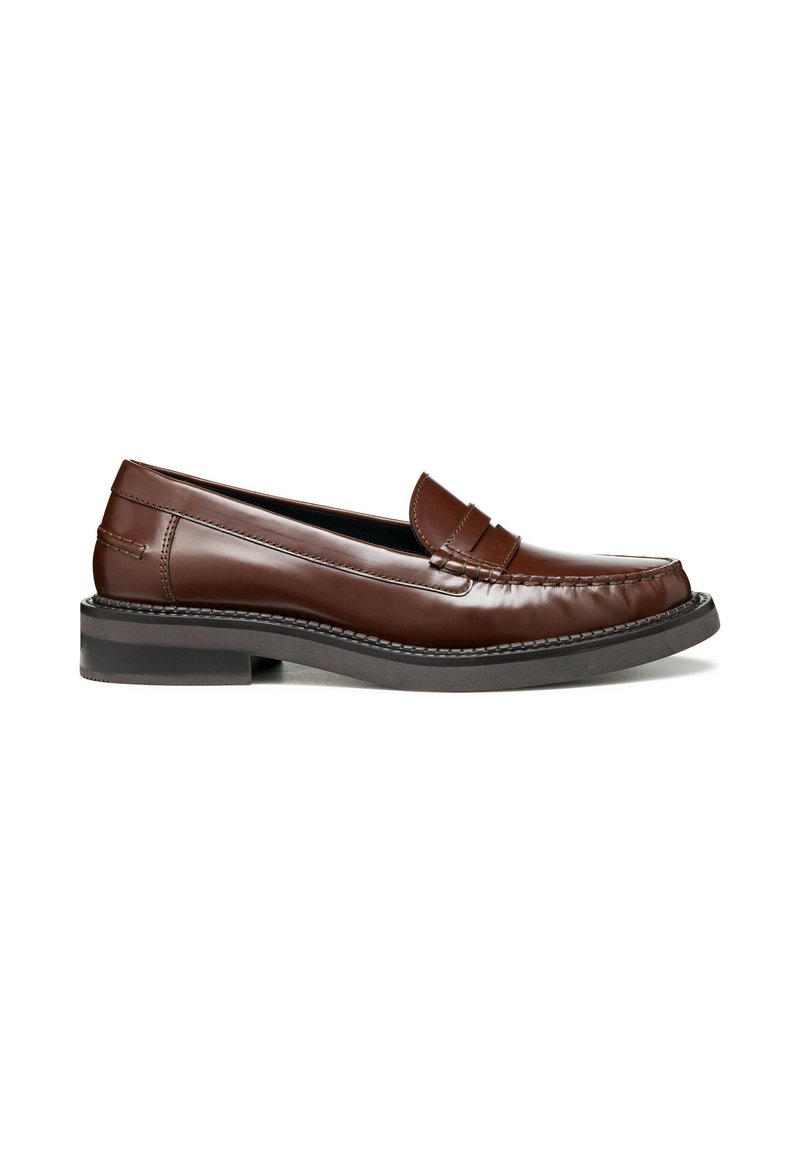 Mocasines de cuero marrón con un acabado suave, con costuras decorativas y suela baja de goma negra. Diseño clásico sin cordones, fácil de poner y quitar.