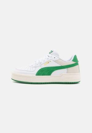 Hvide sneakers med grønne detaljer, der har en glat læderoverdel, perforeringer på tæerne og en tyk cremefarvet sål. Guld logo-detalje på siden.