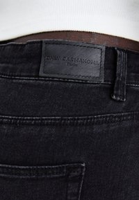 Črne denim hlače z usnjenim oznako "ONLY CARMAKOMA" na pasu. Imajo zadnji žep in subtilne šivanske detajle.