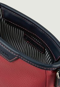 Roter strukturierter Lederbag-Innenraum mit marineblauen Akzenten, ausgestattet mit einem Reißverschlussfach und gestreifter Stoffauskleidung. Markenetikett sichtbar.