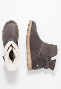 Harmaat mokka nilkkasaappaat, joissa on pehmeä valkoinen vuori, sivussa hihna ja solkiyksityiskohta sekä teksturoitu kumipohja.