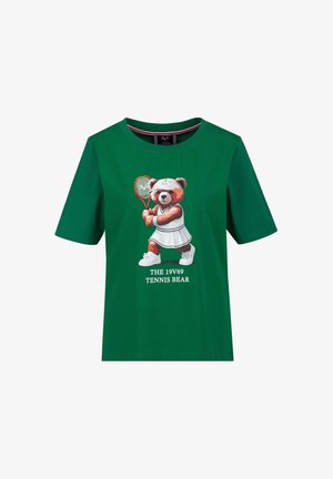 Groen T-shirt met een cartoonbeer gekleed in witte tennisoutfit en een racket vasthoudend, tekst eronder: "THE 19V69 TENNIS BEAR."