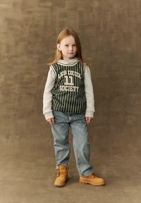 Green and white striped sleeveless hoodie with "LES DEUX SOCIETY" text, paired with blue jeans and tan lace-up boots. Neutral background.