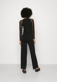 Combinaison noire avec un corsage ajusté et des manches longues transparentes, pantalon à pattes larges et chaussures à plateforme chunky. Tissu lisse avec un design épuré.