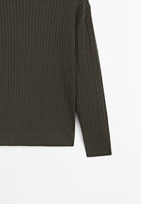 Maglione grigio scuro lavorato a maglia con motivi a trecce testurizzati, polsini e orlo a costine. Il materiale sembra morbido e flessibile.