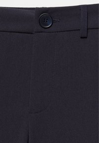 Gros plan de la ceinture d'un pantalon bleu marine foncé avec un bouton noir et une boucle de ceinture, montrant la texture du tissu et les détails de couture.