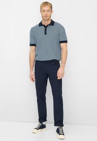 Marineblauw-wit gestreept poloshirt met korte mouwen en een effen kraag, gecombineerd met marineblauwe broek en marineblauwe sneakers met witte zolen.