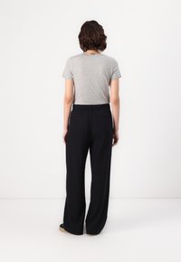 T-shirt gris à manches courtes associé à un pantalon noir taille haute ample. Tissu lisse avec un design simple.