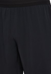 Svarta träningsshorts med elastisk midjeband, visas i närbild med fokus på övre låret och midjeområdet.