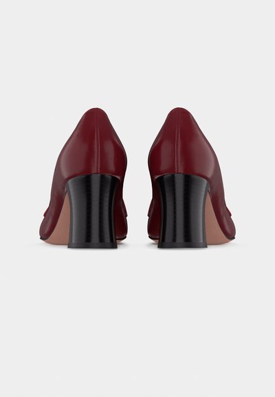 Paire de chaussures en cuir bordeaux à talons blocs, vues de dos avec des talons arrondis et légèrement effilés sur un fond clair.