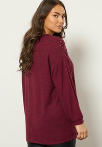 Burgundowa bluza z długim rękawem o fakturowanej tkaninie, z subtelnymi akcentami cekinów na ramionach i luźnym krojem.