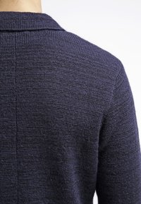 Marinblå stickad tröja med texturerad yta, med krage och detalj på baksidan, sedd från en bakifrån perspektiv.