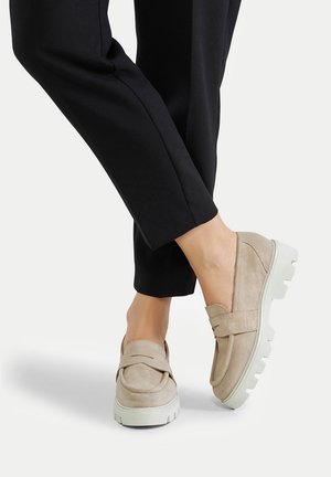 Zapatos beige de ante sin cordones con una suela blanca gruesa, con un diseño superior liso. Combinados con pantalones negros a medida.