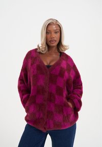 Měkký pletený svetr s knoflíky v kostkovaném vzoru magenta a bordó barvy, s výstřihem do V, zapínáním na knoflíky a dvěma bočními kapsami.