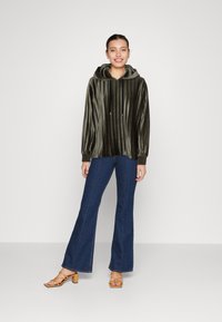 Felpa con cappuccio in velluto verde scuro, decorata con pieghe verticali, abbinata a jeans in denim scuro a zampa d'elefante e sandali con tacco a blocco marroni.