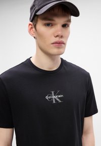 T-shirt de algodão preta com um logótipo prateado da Calvin Klein no peito. Mangas curtas e design de gola redonda.