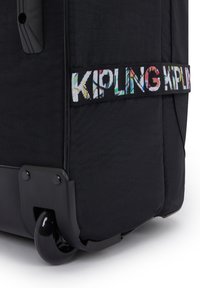 Zwarte rolkoffer met textuurvlies, voorzien van een kleurrijk Kipling-logo op een lint en duurzame zwarte wielen.