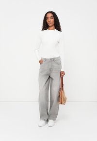 Jeans de pernera ancha de color gris claro, hechos de denim, combinados con una blusa ajustada de manga larga blanca. Incluye zapatillas blancas y un pequeño bolso marrón claro.