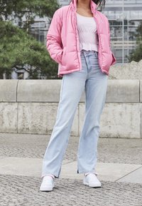 En rosa puffjacka över en vit smockad crop top, tillsammans med ljusblå utsvängda jeans och vita sneakers med pastellaccent.