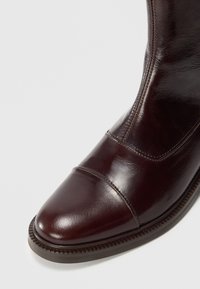Bottine de costume en cuir poli brun foncé avec un bout arrondi, des coutures visibles et une semelle épaisse à nervures, sur fond blanc.