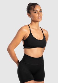 Zwarte sportbh met dunne bandjes en een naadloos ontwerp, gecombineerd met zwarte high-waisted shorts. Glad, rekbaar materiaal.
