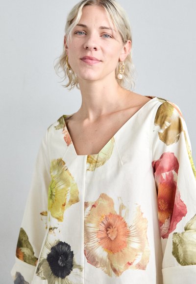Blusa de flores en color crema, con mangas oversized y un escote en V profundo. Los colores incluyen amarillo, naranja, rosa y acentos en negro.