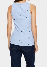 Ljusblå ribbad tanktopp med små svarta hjärtdesigner utspridda, rund halsringning och utan ärmar. Matchas med mörka jeans.