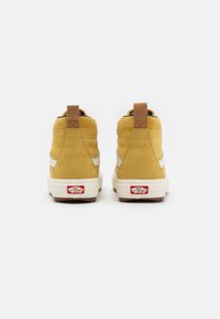 Sneaker alte in suede giallo con striscia laterale bianca, suole in gomma marrone e etichetta sul tallone rossa con logo. Cuciture rinforzate e dettaglio con linguetta.
