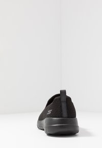 Scarpe slip-on nere in rete con una tomaia testurizzata, suola ammortizzata e un'etichetta sul retro per indossarle facilmente. Design minimalista, senza marchio visibile.