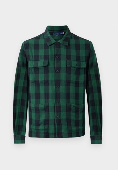 Camisa xadrez verde e preta, feita de tecido com fecho frontal de botões, duas bolsas no peito e mangas longas com punhos abotoados.
