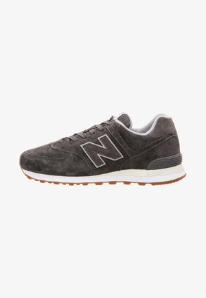 Baskets New Balance en daim gris foncé avec semelle intermédiaire blanche, semelle extérieure en gomme et logo "N" bien visible sur le côté.