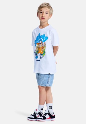 Wit katoenen T-shirt met kleurrijke cartoonafbeelding, gecombineerd met licht denim short, zwarte en rode sneakers, en witte sokken met logo.