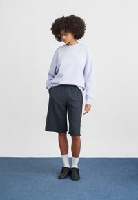 Világos lila pulóver, laza szabással, sötétszürke, térd alá érő rövidnadrággal párosítva. Fehér térdzoknik és fekete cipők teszik teljessé a megjelenést.