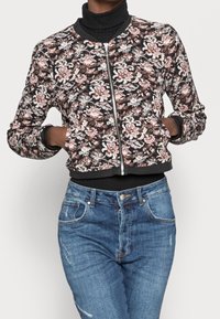 Blumige Bomberjacke mit schwarzem Hintergrund, Reißverschluss vorne, gerippten Bündchen und Saum. Kombiniere sie mit blauen, hoch taillierten Jeans. Weicher Stoff, lebendiges Design.