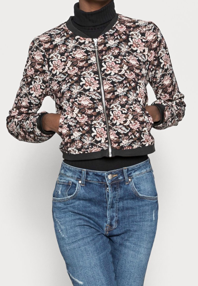 Blumige Bomberjacke mit schwarzem Hintergrund, Reißverschluss vorne, gerippten Bündchen und Saum. Kombiniere sie mit blauen, hoch taillierten Jeans. Weicher Stoff, lebendiges Design.