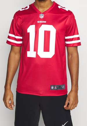 Person iført en rød San Francisco 49ers NFL-trøje med nummer 10, hvide striber på ærmerne og sorte Nike-shorts.