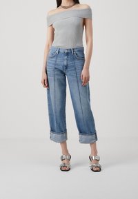 Top gris acanalado de un solo hombro, jeans cortos azul claro con dobladillos enrollados y sandalias con hebilla plateada. Conjunto simple y casual con texturas variadas.