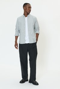 Camisa de manga larga azul claro con botones sobre una camiseta blanca, combinada con pantalones negros de corte holgado y zapatos negros con cordones.