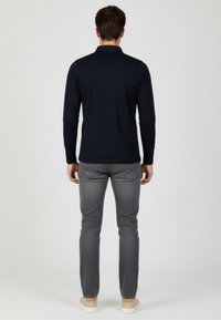 Granatowa bluzka z długim rękawem i kołnierzykiem, zestawiona z jasnoszarymi jeansami o dopasowanym kroju oraz jasnymi trampkami, widziana od tyłu.