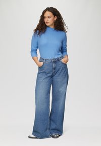 Hellblaues, rippenstricklangärmliges Oberteil und hoch geschnittene, weit geschnittene Jeans aus Denim. Das Outfit zeichnet sich durch eine klassische Passform und eine glatte, weiche Textur aus.
