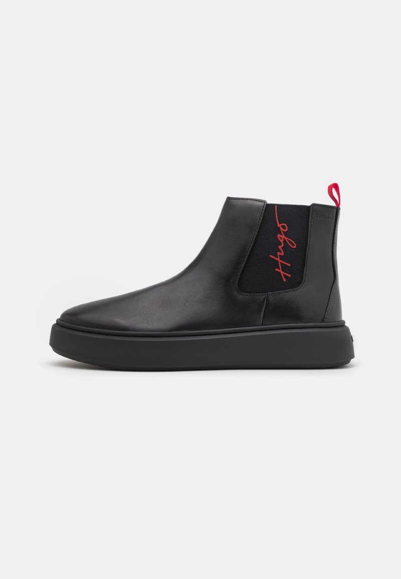Botte Chelsea en cuir noir avec semelle épaisse, panneau latéral élastique avec inscription rouge « Hugo » et languette rouge au talon.